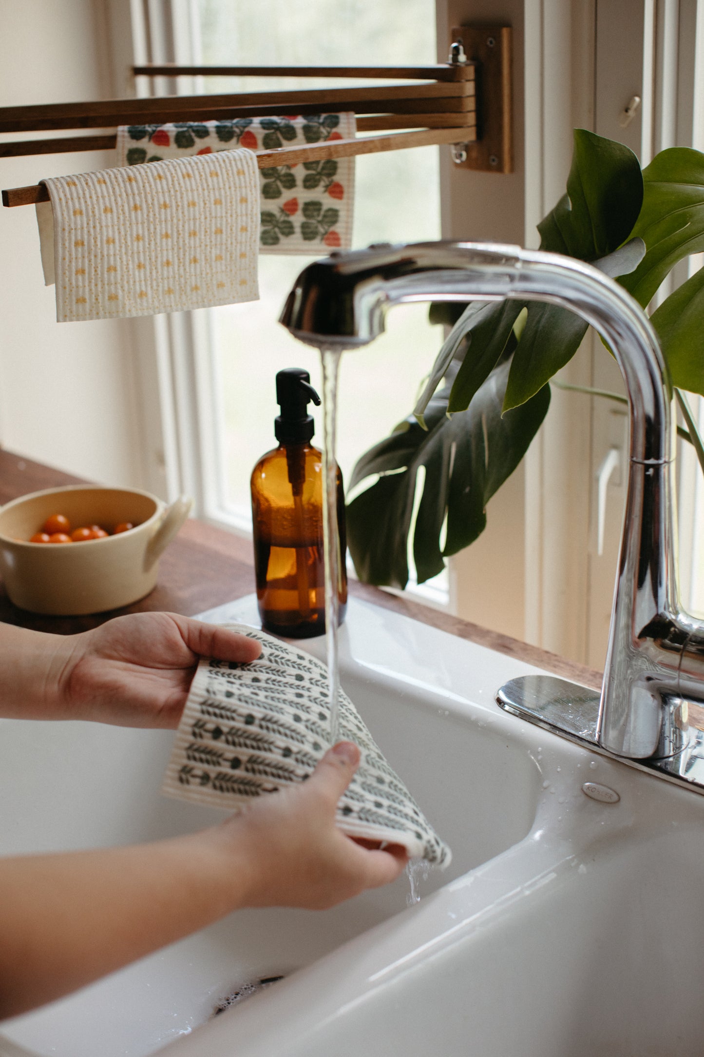 Oak wood towel drying rack holding Swedish Dishcloths while someone wets a dishcloth in the kitchen sink.