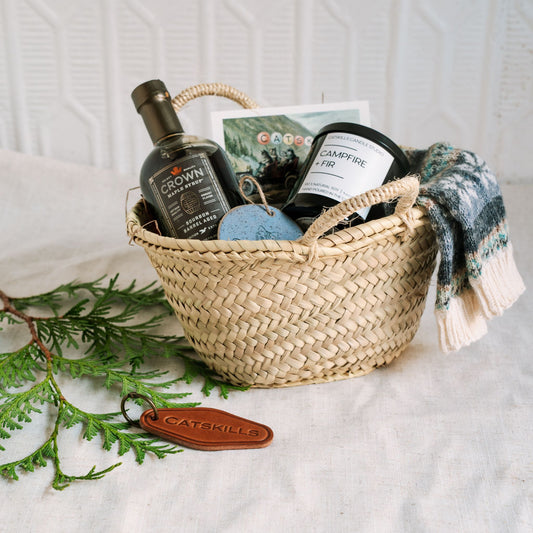 Woven basket with syrup, socks, a postcard and a leather keychain with a light background and greenery.
