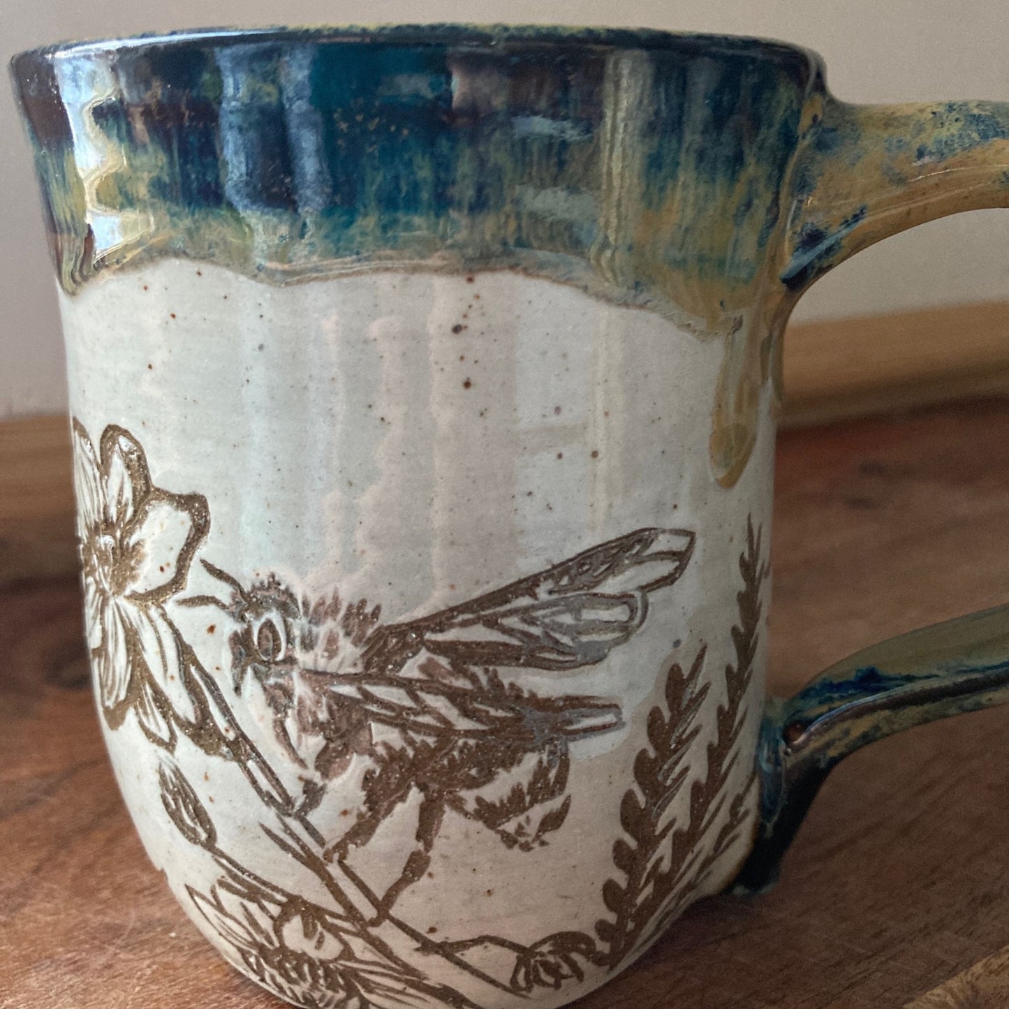 Ceramic mug with bee and floral design on a wooden surface
