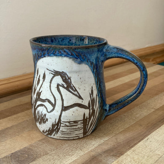 Ceramic mug with blue rim and handle, featuring a crane design on a wooden surface.
