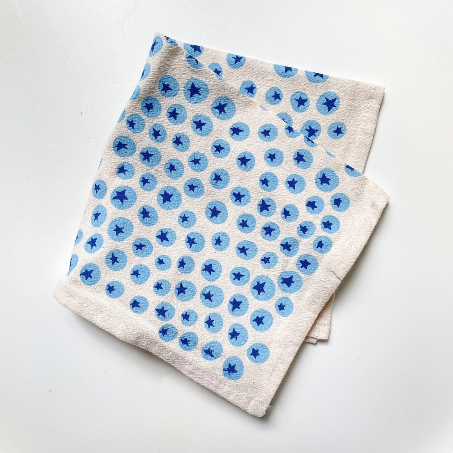 Stack of white cloth napkins with blueberry pattern on a white surface