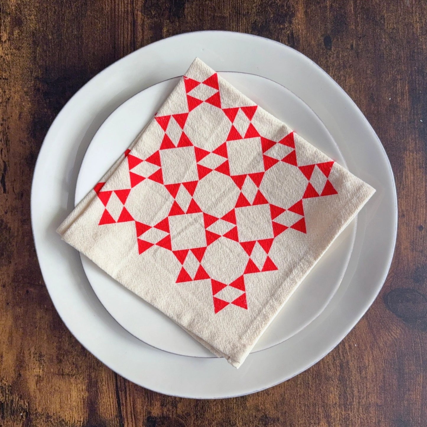 Folded napkin with red geometric pattern on a white plate on a wooden table
