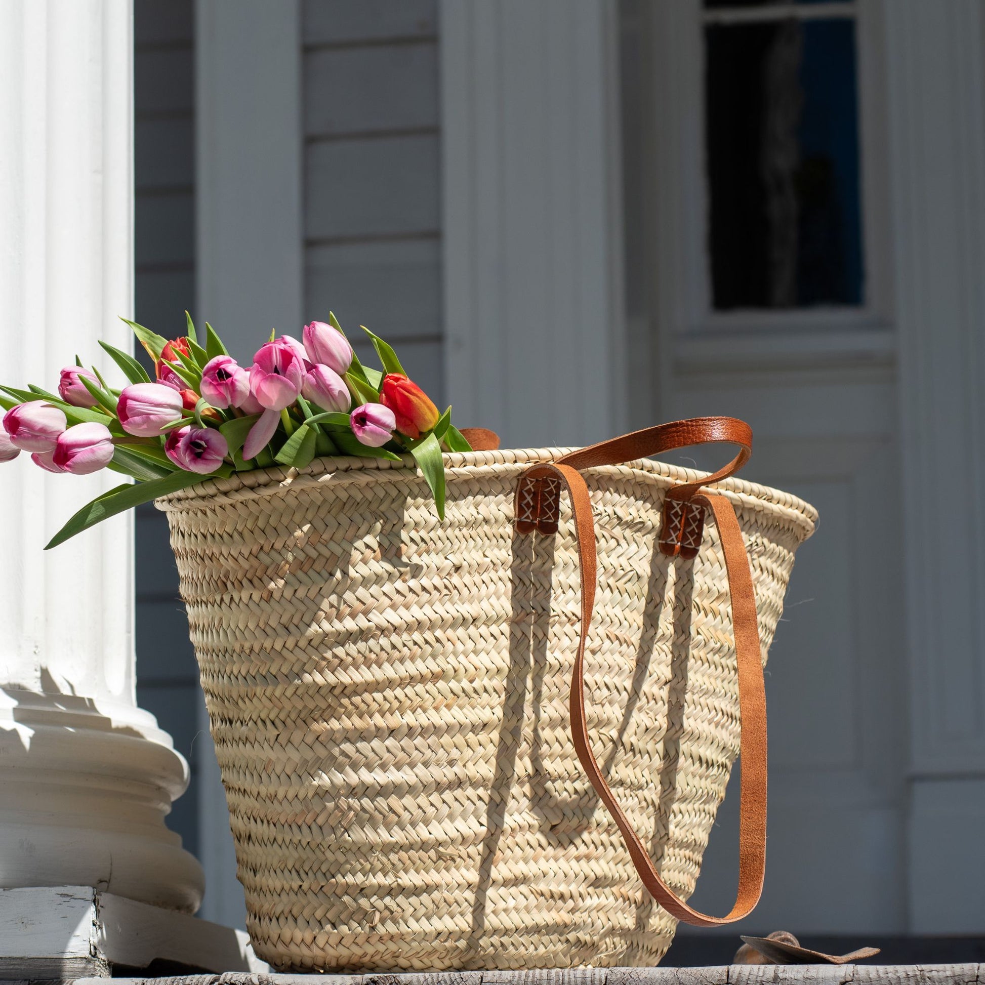 A french market tote on a porch filled with tulips