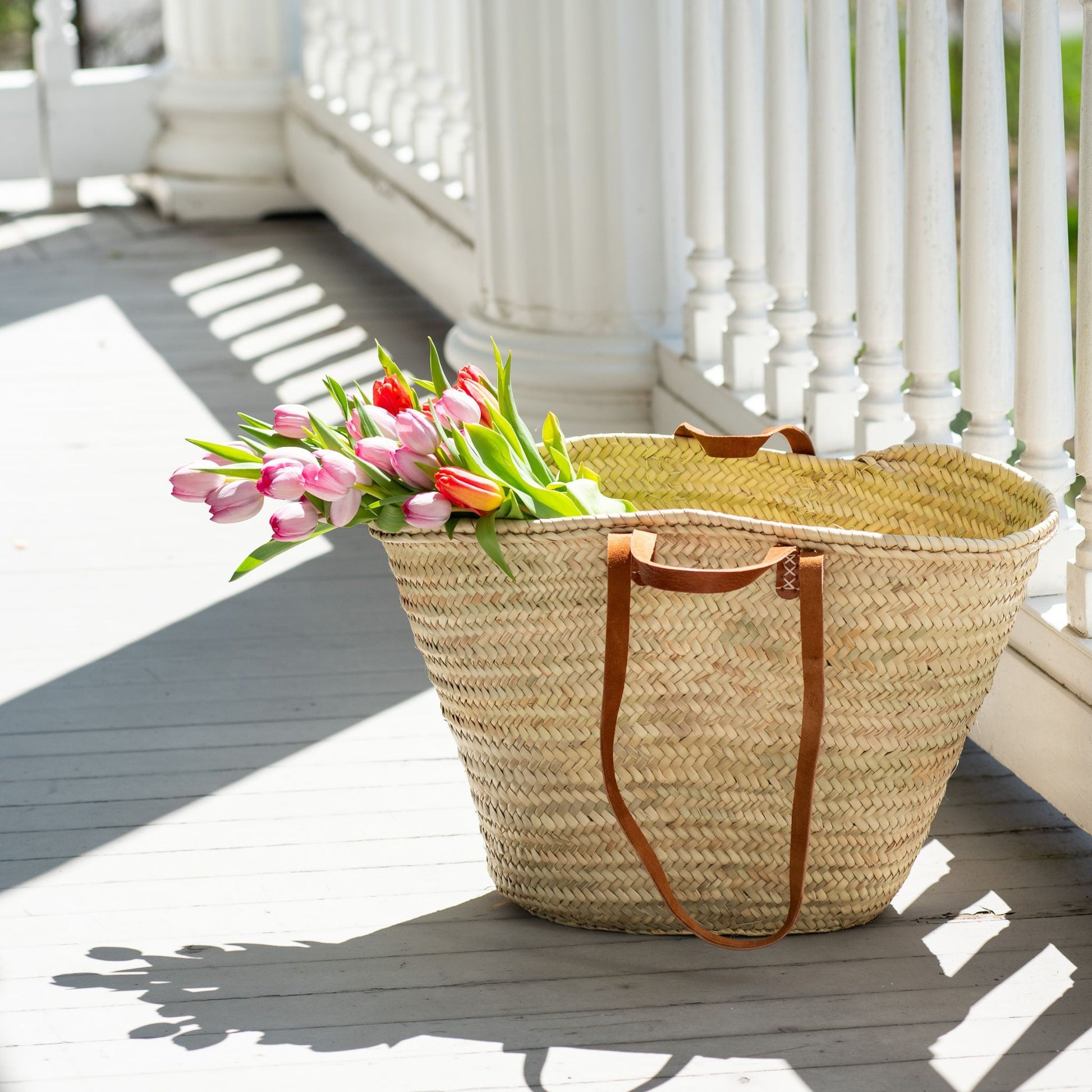 French market tote bag with leather straps holding tulips on an outside porch
