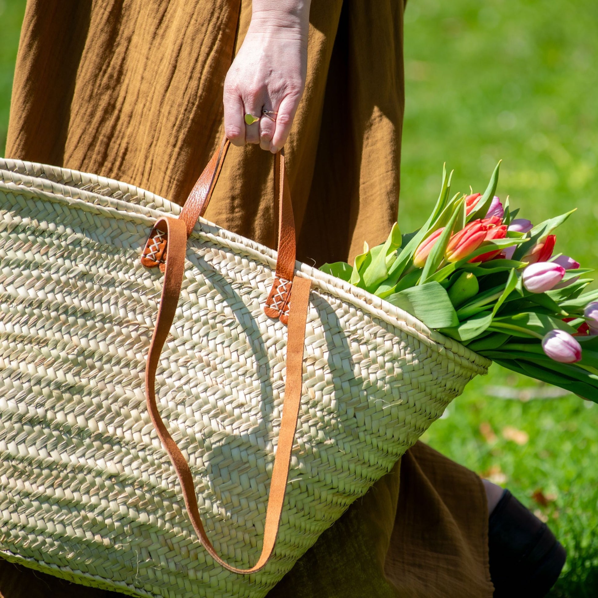 A woman carrying a french market tote bag with leather straps filled with tulips