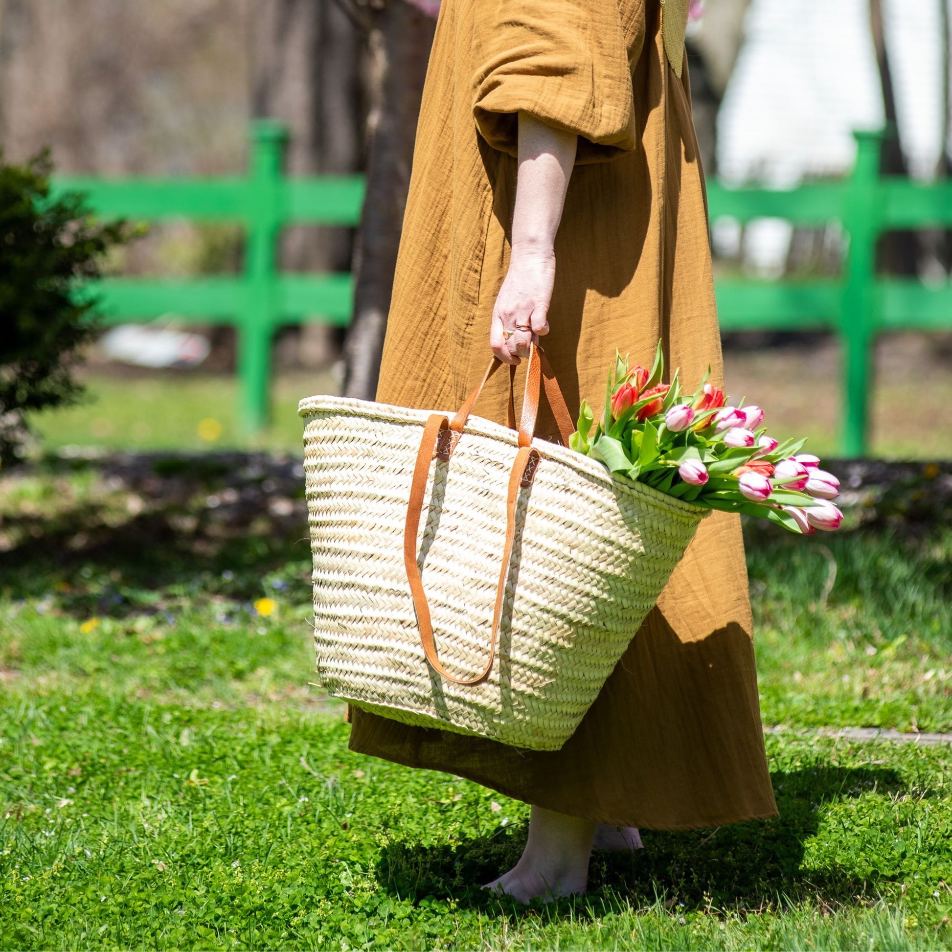 A woman carrying a french market tote bag with leather straps filled with tulips