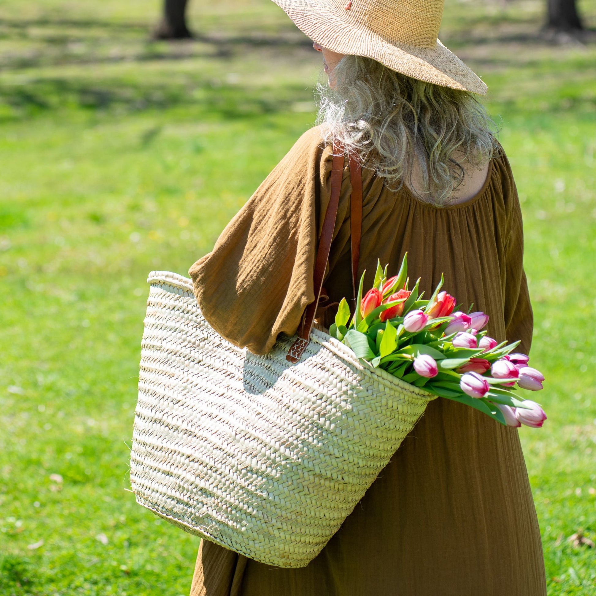 A woman carrying a french market tote bag with leather straps filled with tulips