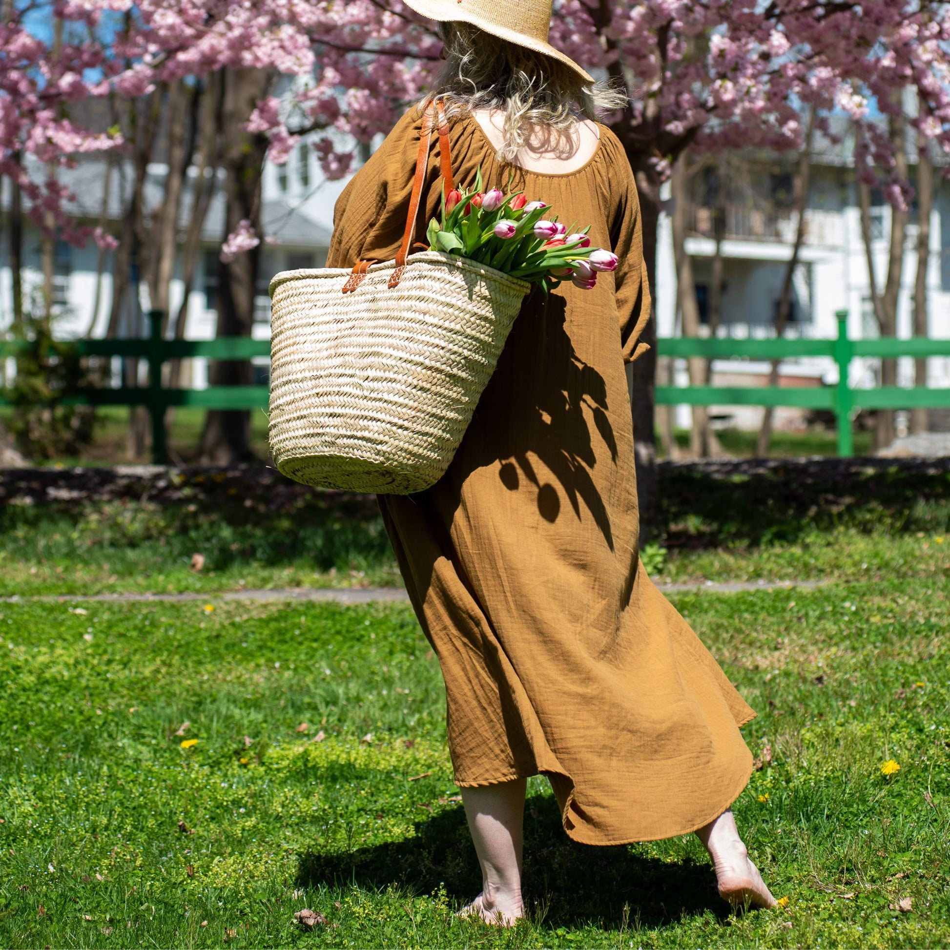 A woman carrying a french market tote bag with leather straps filled with tulips