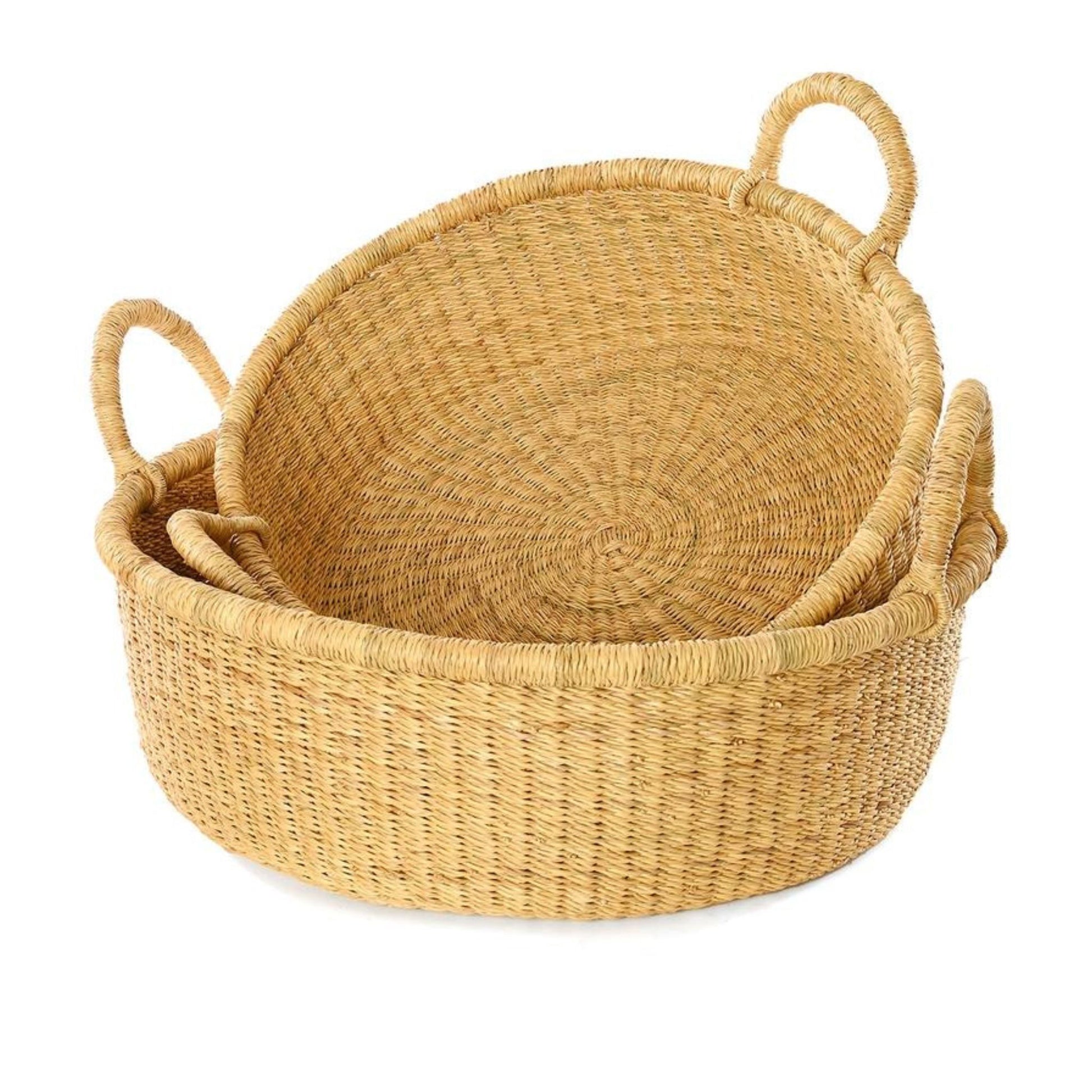 A shallow, tan, woven storage basket with handles and a smaller version inside of it leaning against the side.