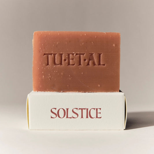 Red brown soap bar with TU.ET.AL on it sitting on a white box that says solstice.