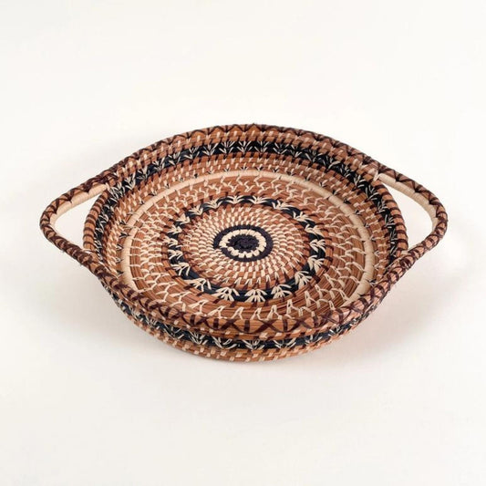 Shallow, round, pine needle tray basket with handles. It has a brown, black, and tan woven design on the top.