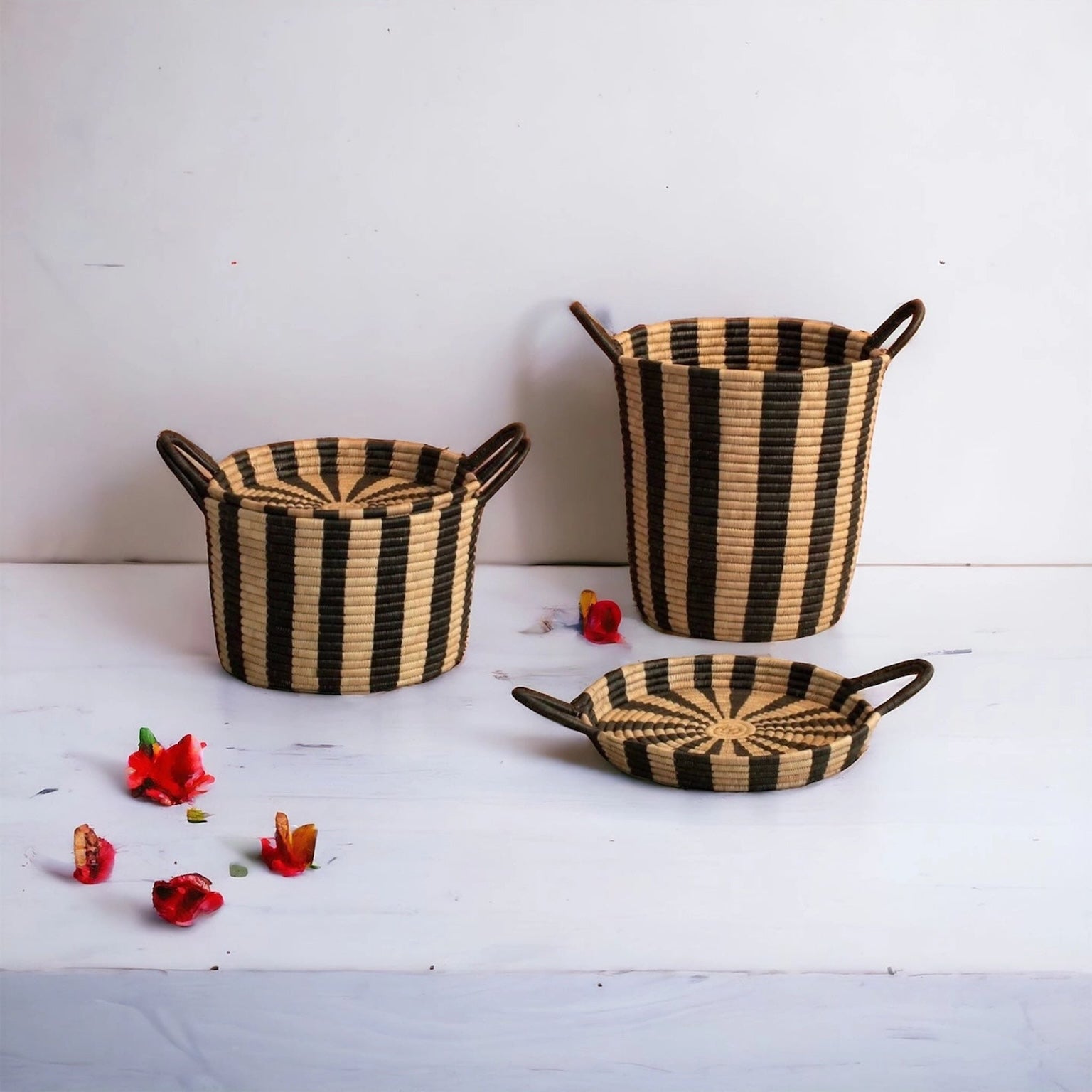 Black and tan striped storage baskets in large and small with a white background and red flowers. The small basket has its lid on and the large ones lid is in front of it.
