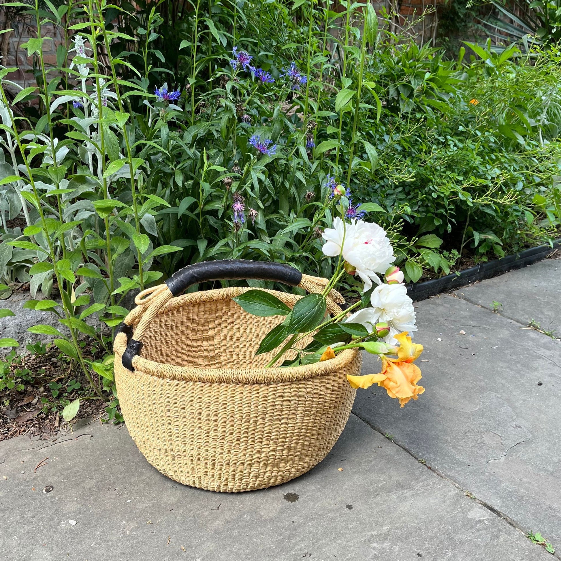 Large bolga basket with a black leather handle holding flowers outside