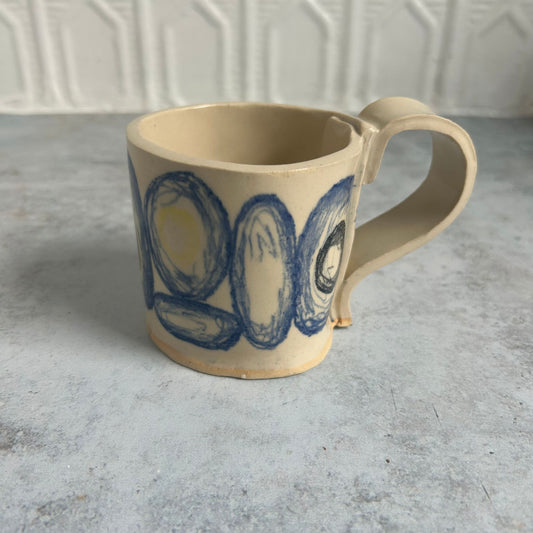 A white mug with blue circles and yellow and black smaller circles within each blue one.