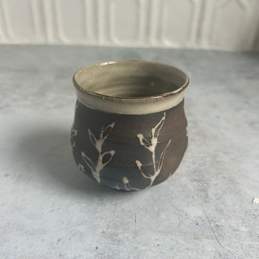 Small brown cup with a white vine pattern along the sides and a white inside.