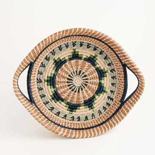 Overhead view of shallow, round, pine needle tray basket. It has a blue, green, and tan woven design on the top.
