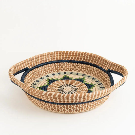 Side view of shallow, round, pine needle tray basket. It has a blue, green, and tan woven design on the top.