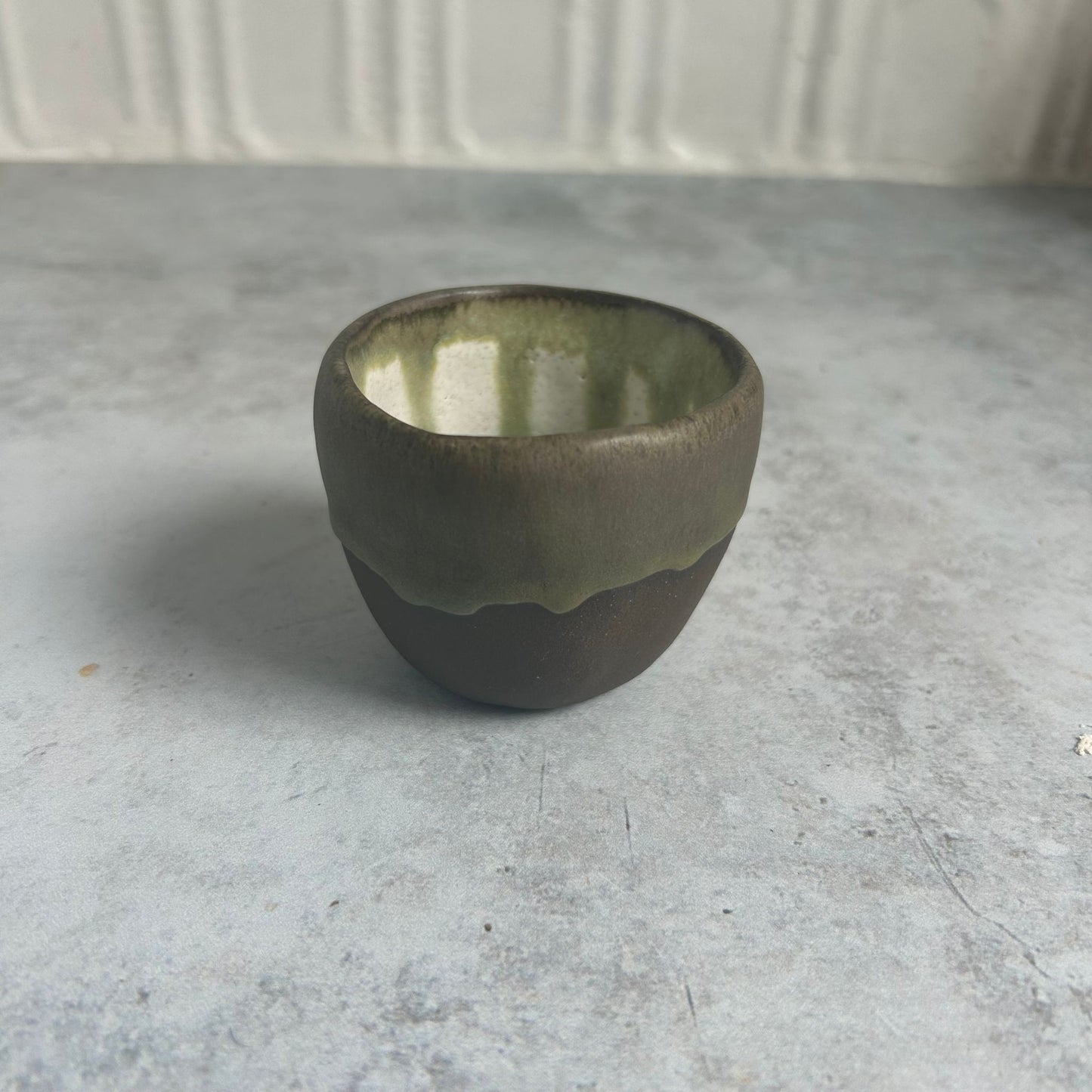 A small brown cup with a white and green drip inside.