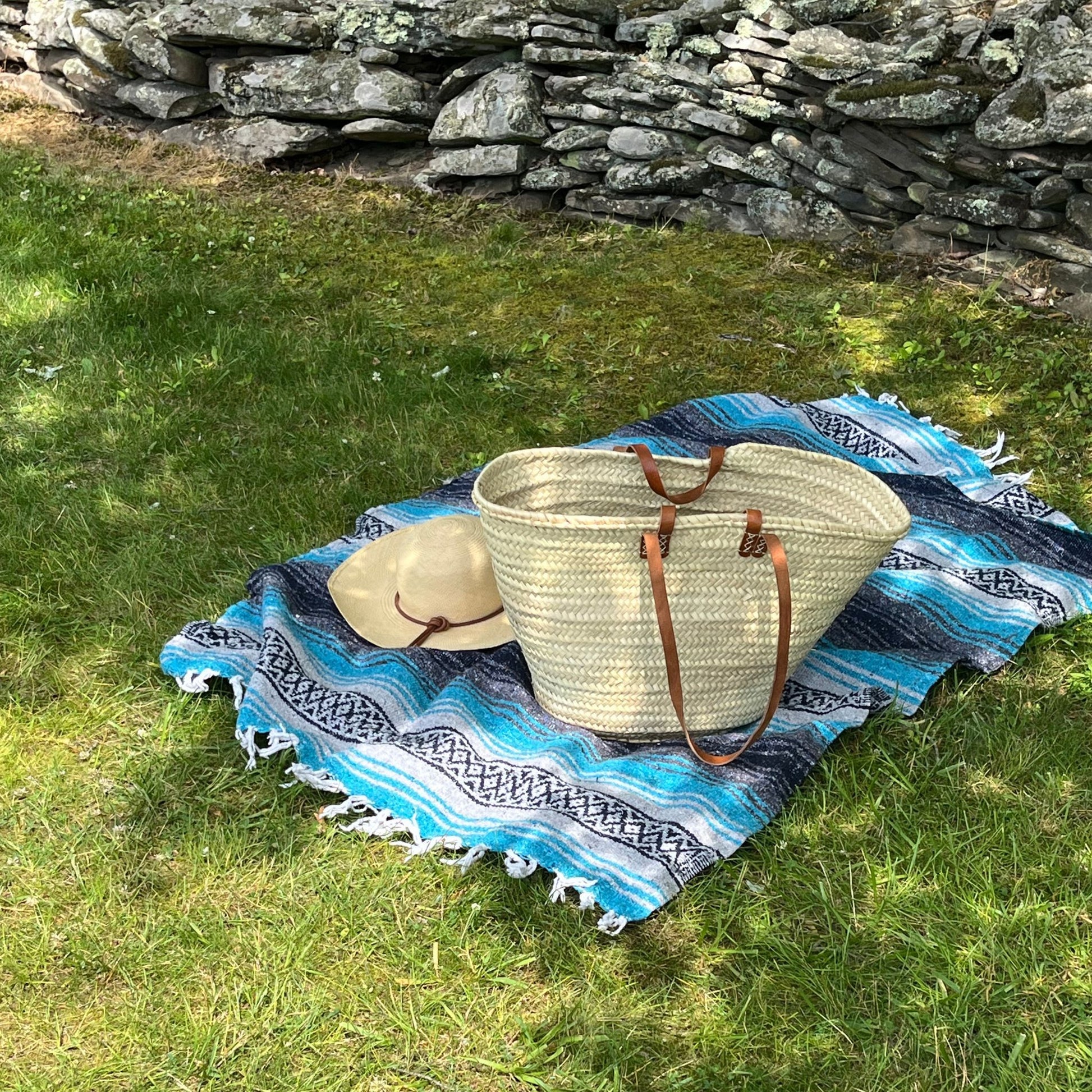 A french market tote on a picnic blanket next to a hat