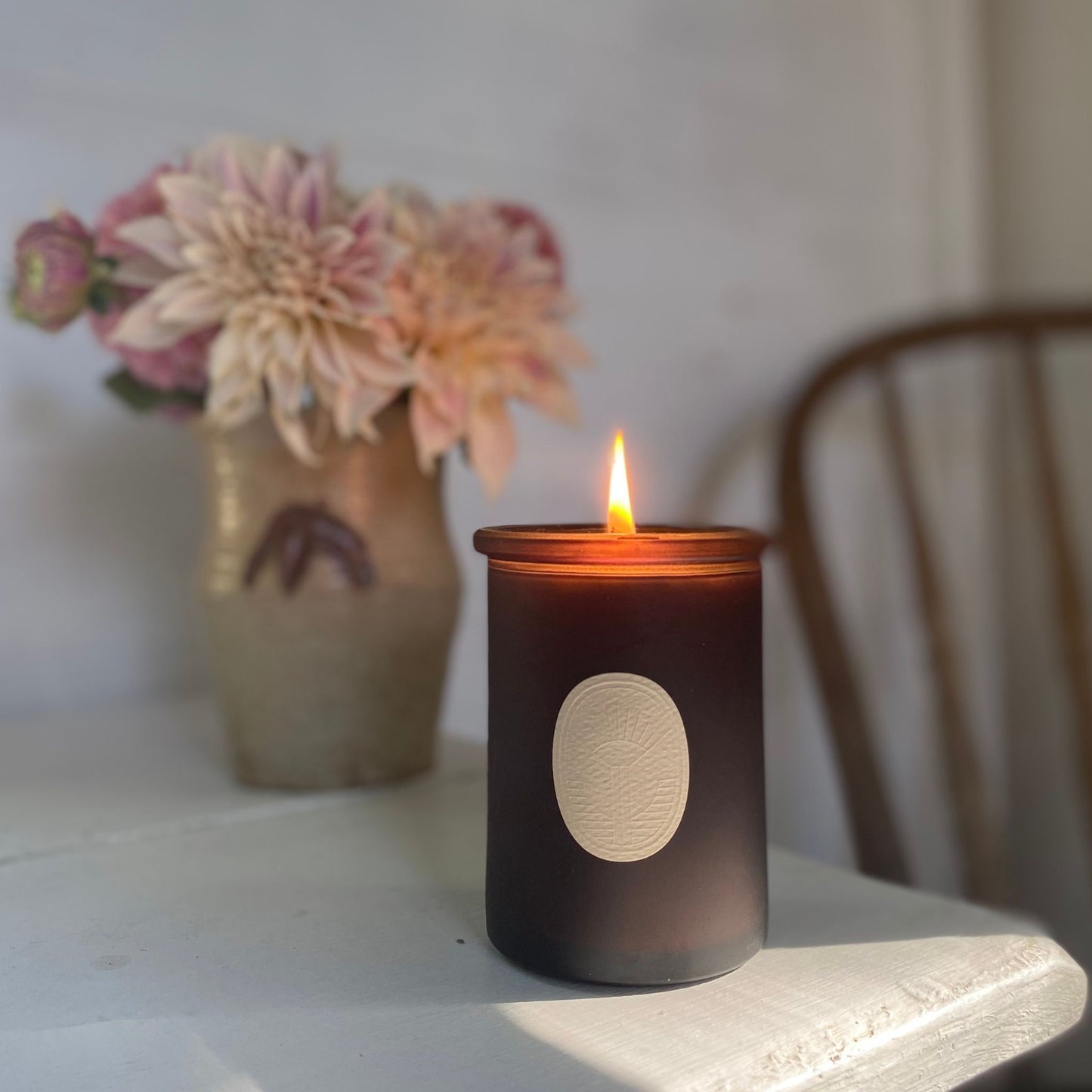 Arboretum Essential Oil Candle on a shelve with a flower bouquet in the back