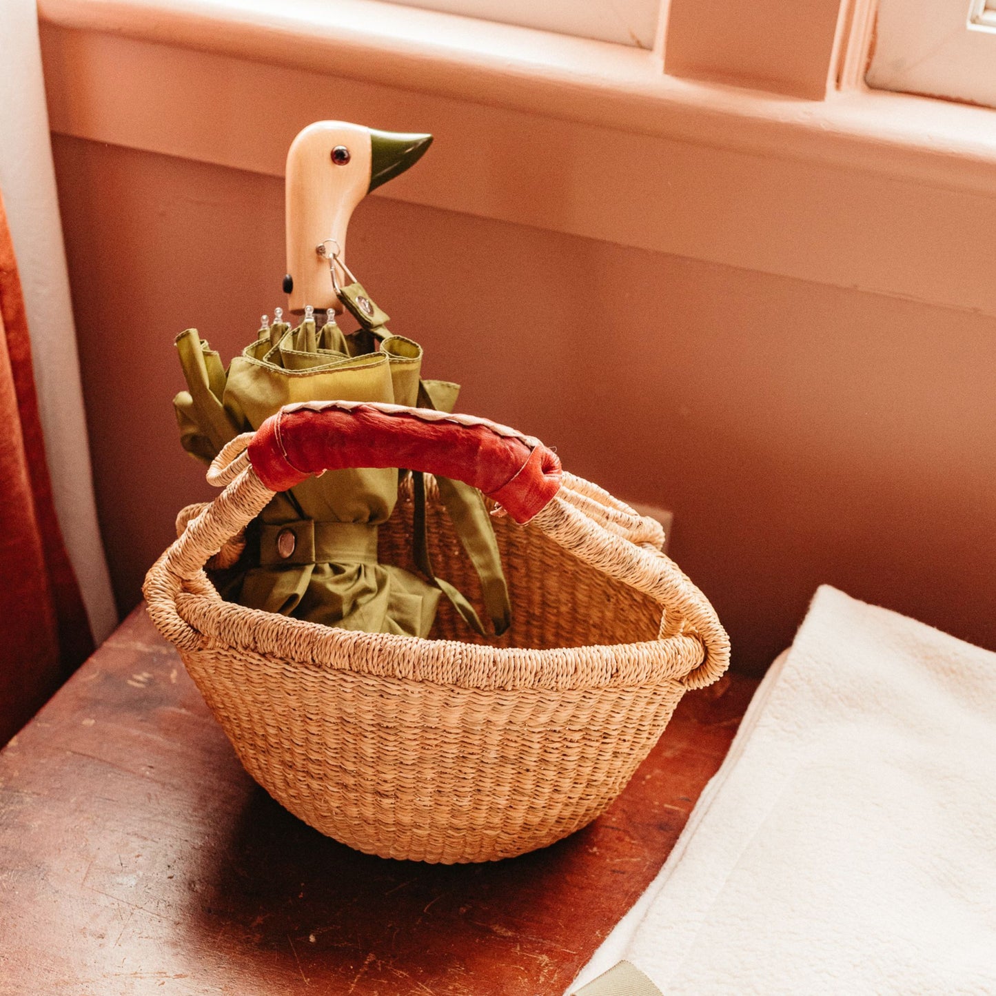 umbrella in olive with birchwood handle in the shape of duck head resting in a basket