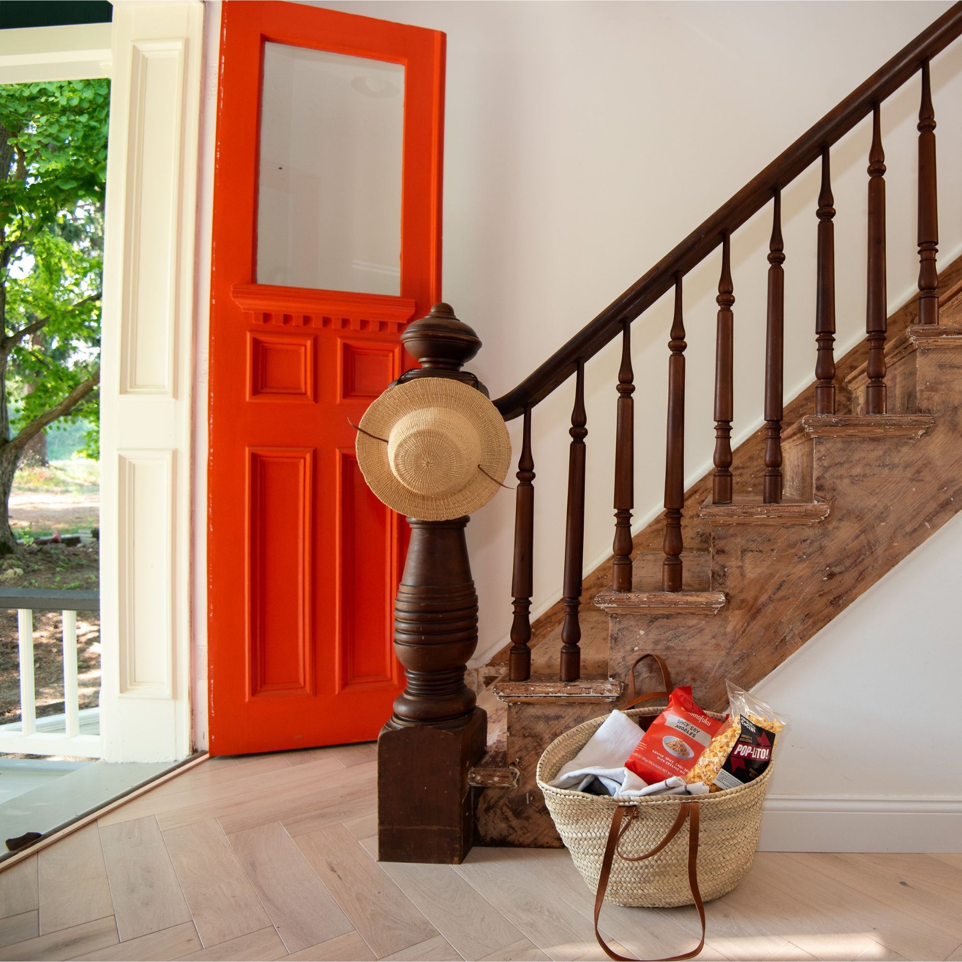 A french market tote bag with leather straps at the bottom of a staircase in a homes entryway.