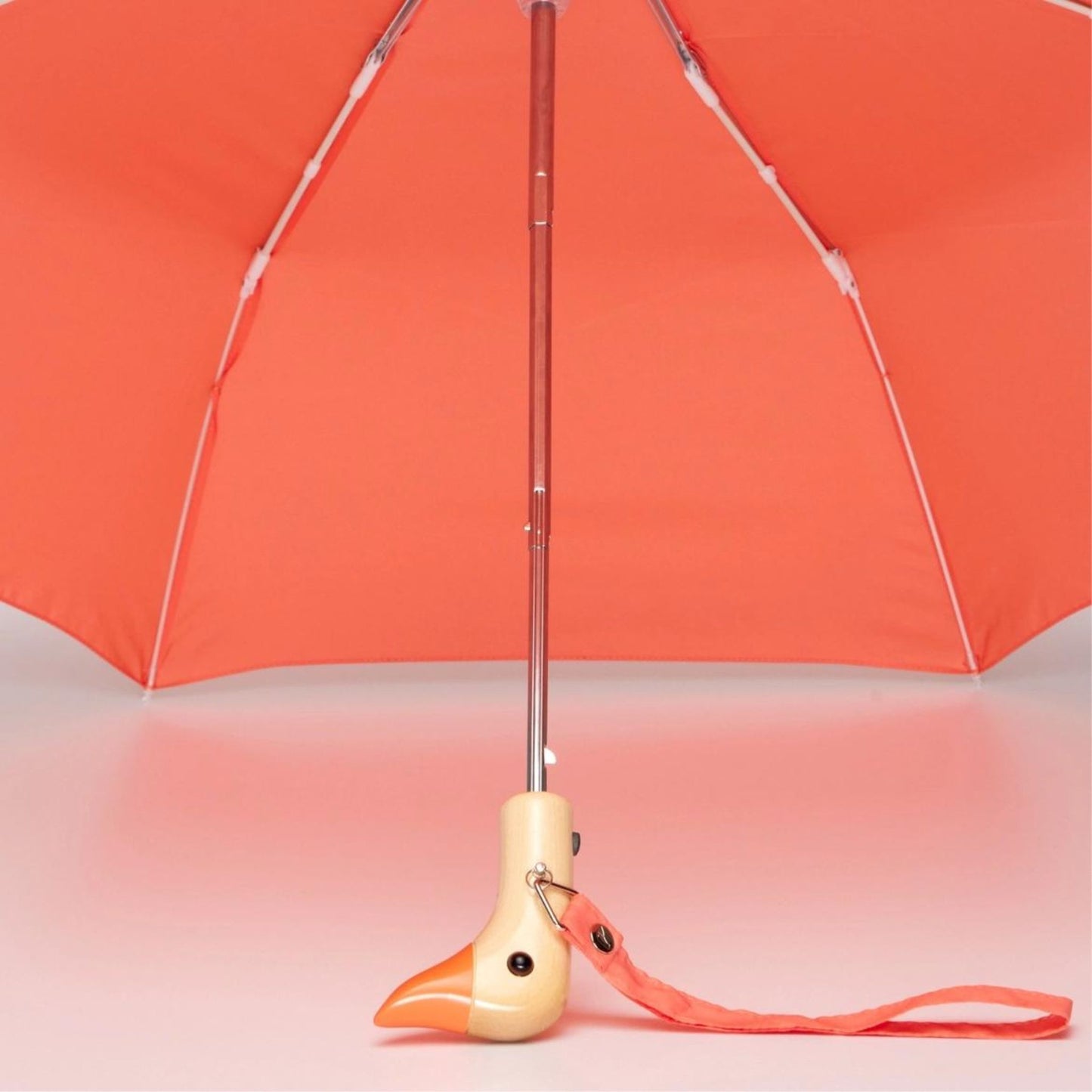 Wide open umbrella in peach with birchwood handle in the shape of duck head