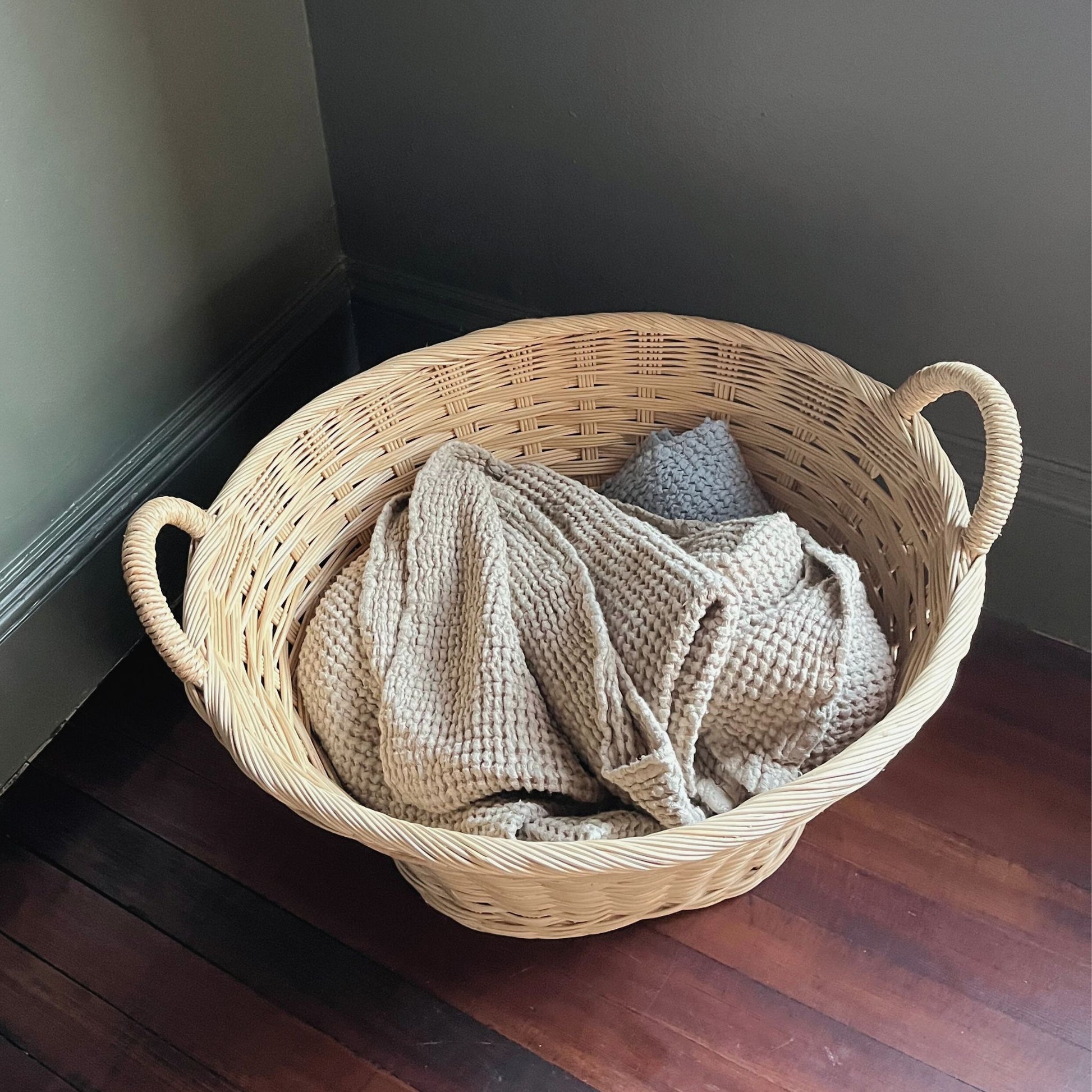 rattan laundry basket filled with linens in a bedroom corner