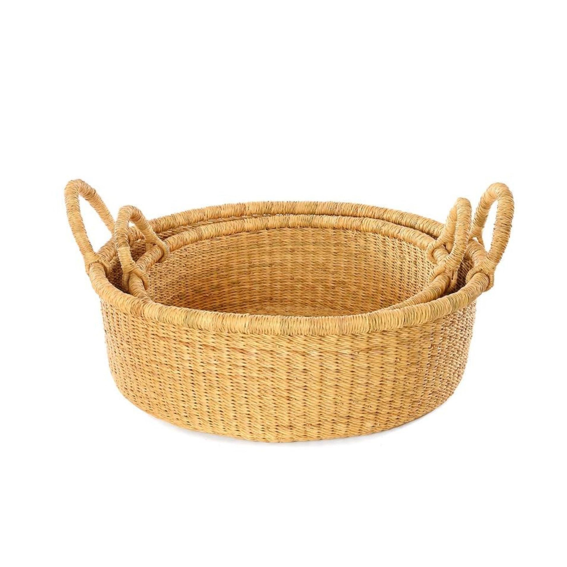 A shallow, tan, woven storage basket with handles with a smaller one inside of it.