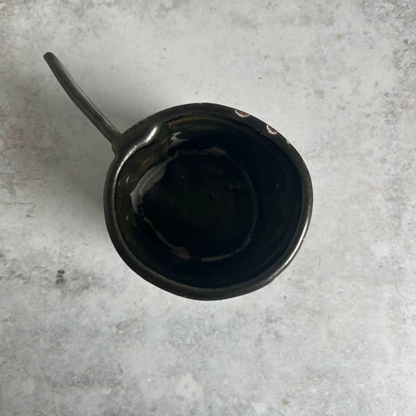 The inside of a black, green, white, and red patterned mug with a triangle handle.