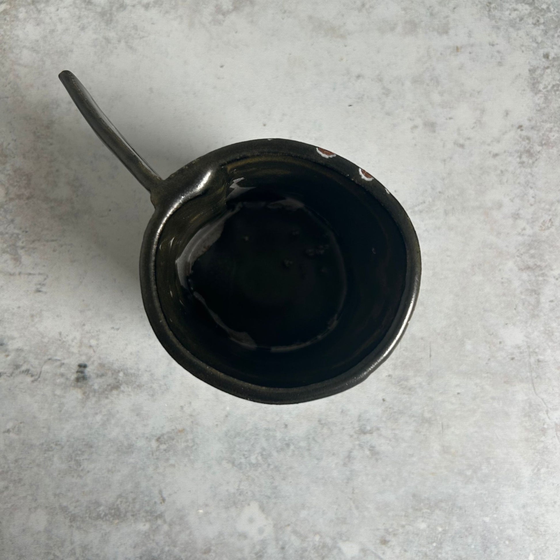 The inside of a black, green, white, and red patterned mug with a triangle handle.
