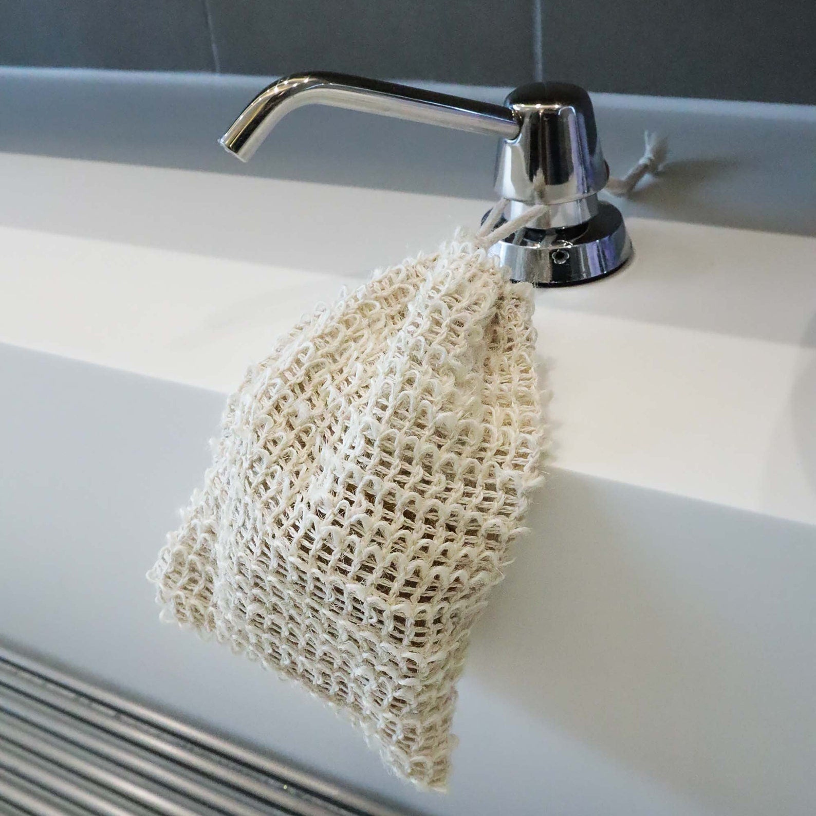 Exfoliating soap saver bag made of sisal with drawstring shown hanging at sink