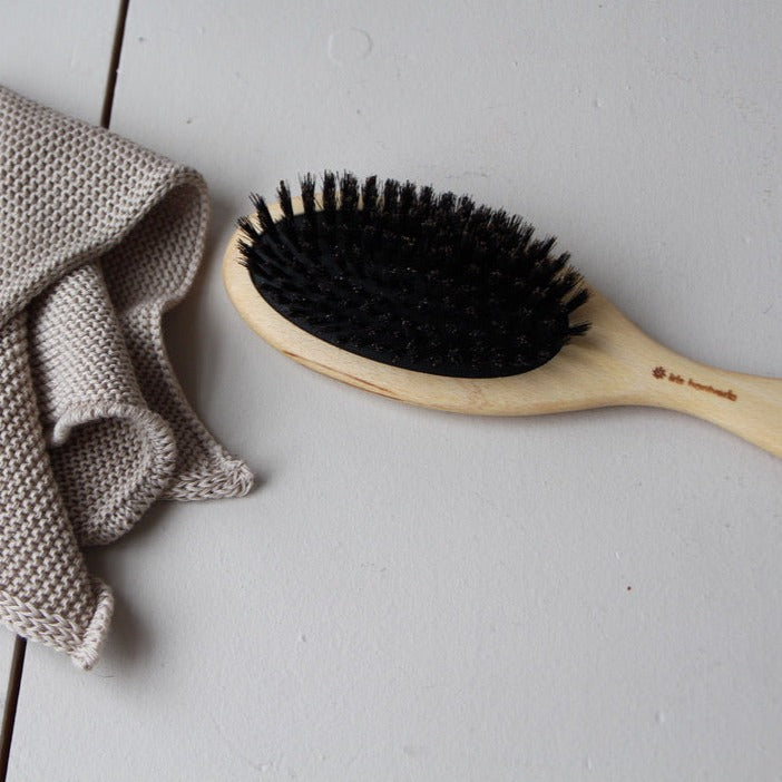 A beech wood hairbrush with wild boar bristles and a cushion in natural rubber next to a towel.