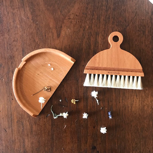 A wooden tabletop crumb brush holding dried flowers