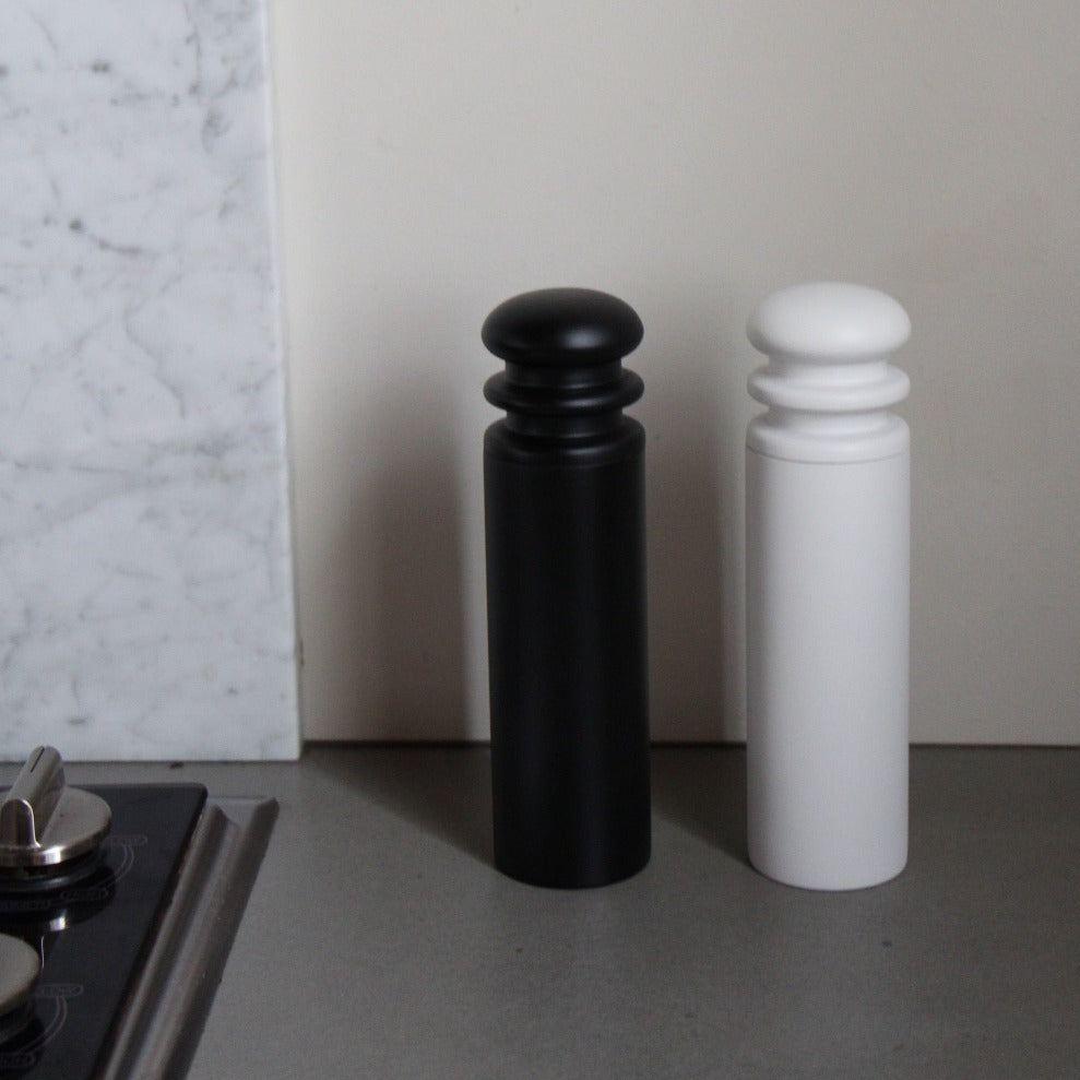 A black and a white salt or pepper mill grinder on a kitchen counter.
