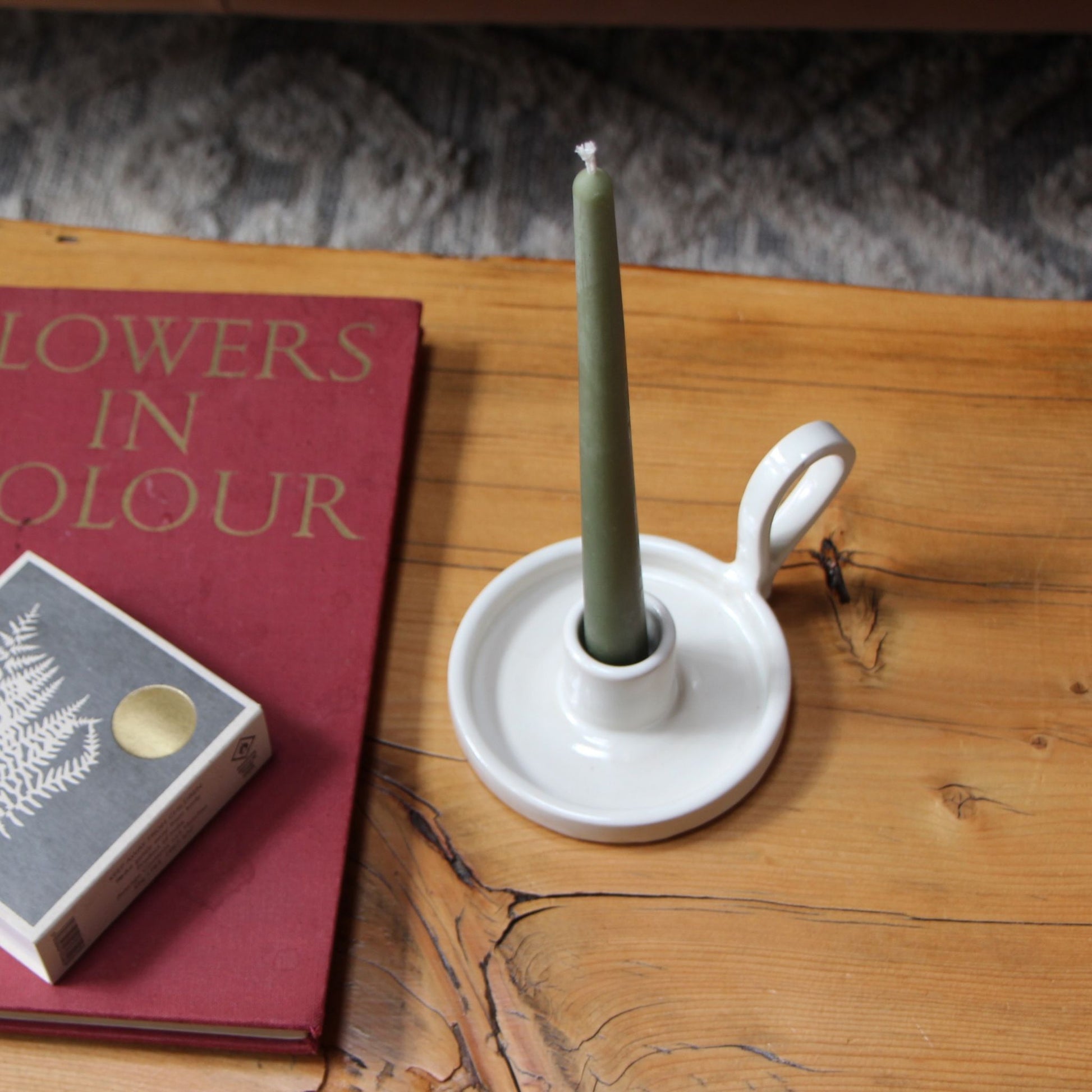 Square box of long wooden matches sitting on a book beside a candle in a ceramic candle holder