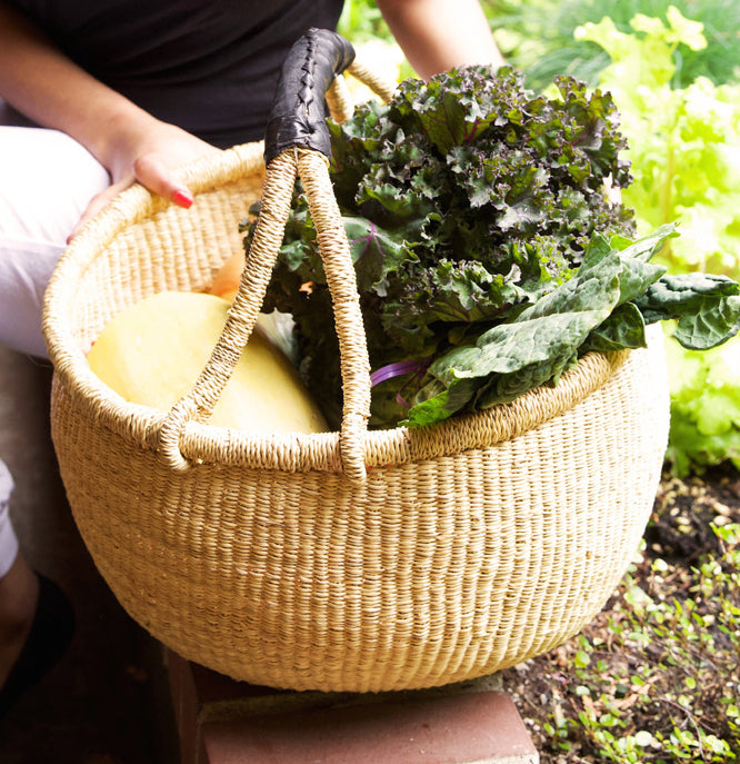 Large bolga basket with a black leather handle holding vegetables
