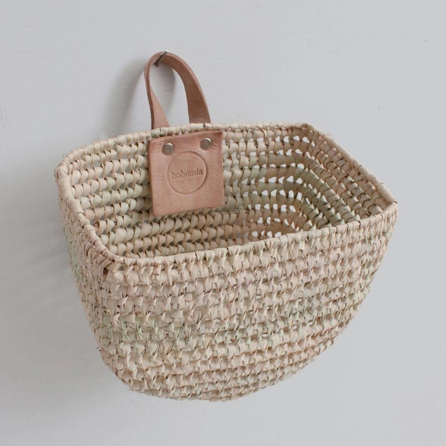 A rounded bottom basket with leather handle hanging from the wall.