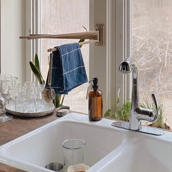 Oak wood towel drying rack with a dish brush and towel hanging from it over a kitchen sink