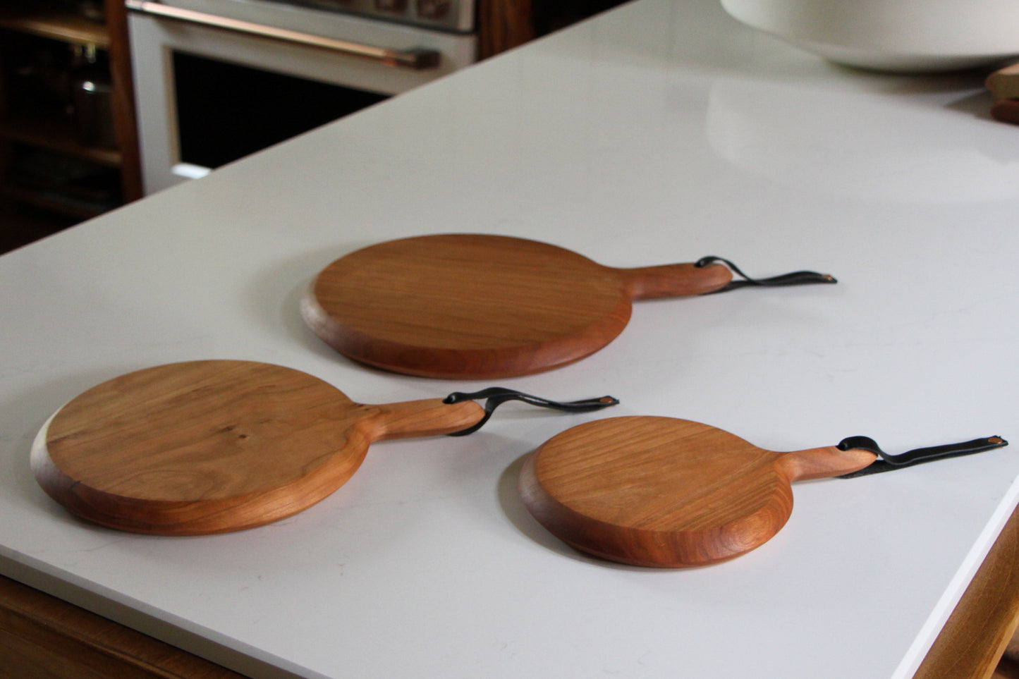 X-Large, large, and medium circular cutting boards in cherry with handle and leather strap