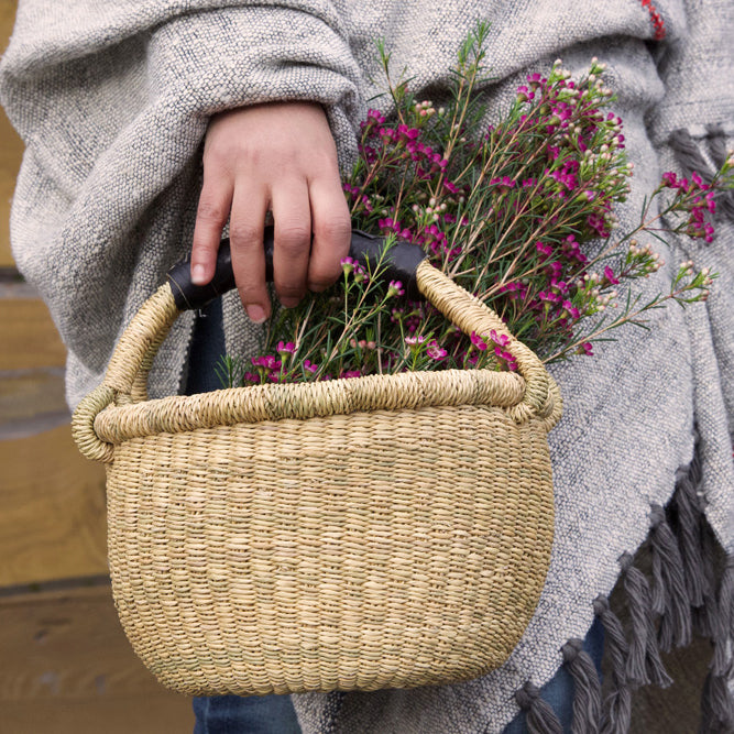 A woman holding a mini round bolga basket with a black leather handle holding flowers
