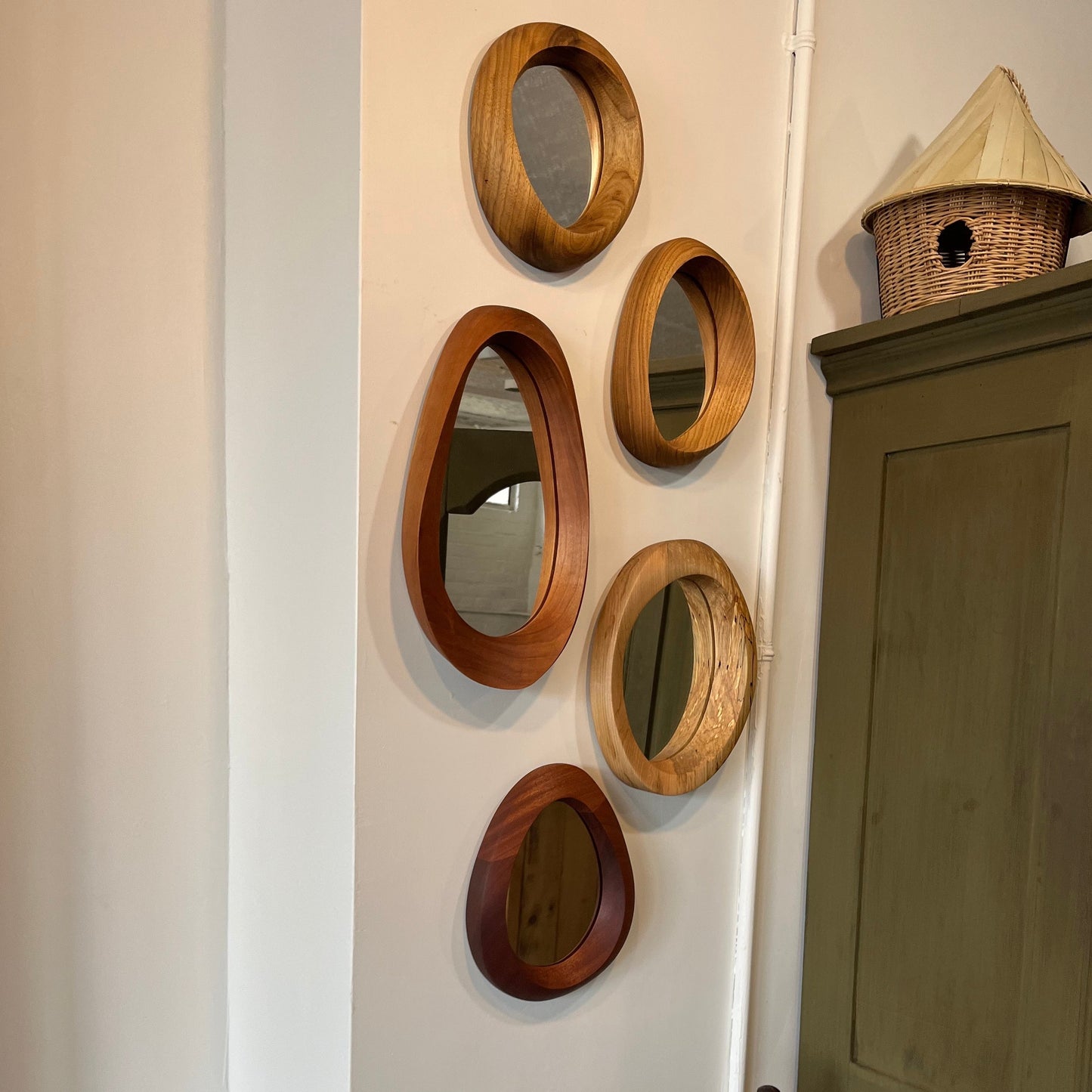 various sizes of hand-carved wooden wall mirrors each with one-of-a-kind organic shape and curves shown in butternut cherry and walnut
