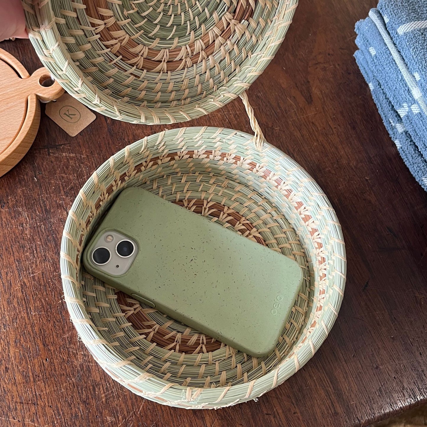 A green and brown 8" x 2.5" lidded basket storing a phone.