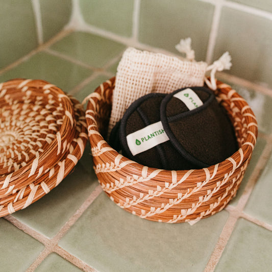 Small woven pine needle lidded basket holding face rounds on green tile.