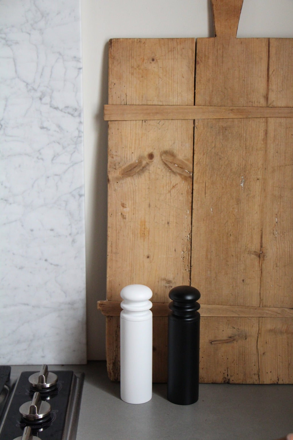 A black and a white salt or pepper mill grinder on a kitchen counter with a wooden cutting board behind them.