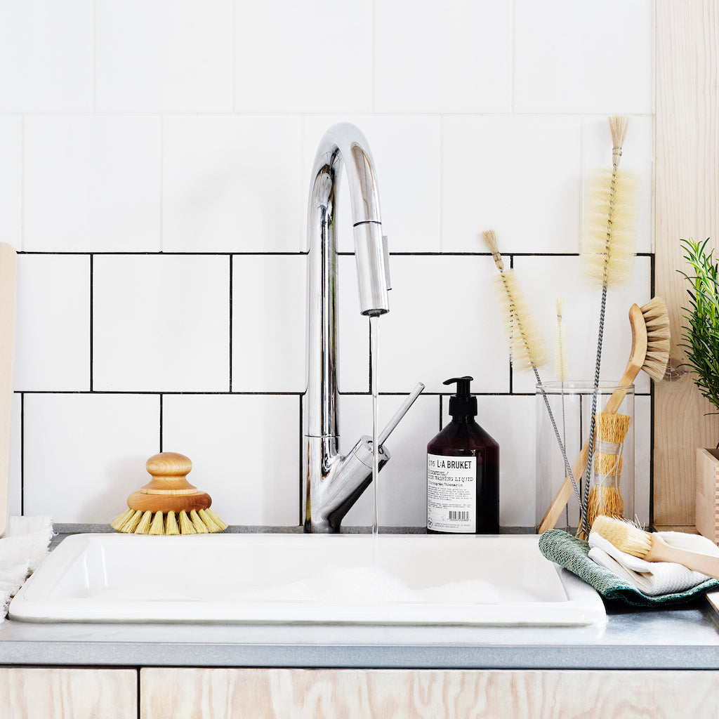 Narrow and long cleaning brushes with bristle tip shown in jar on countertop with handled dish brush