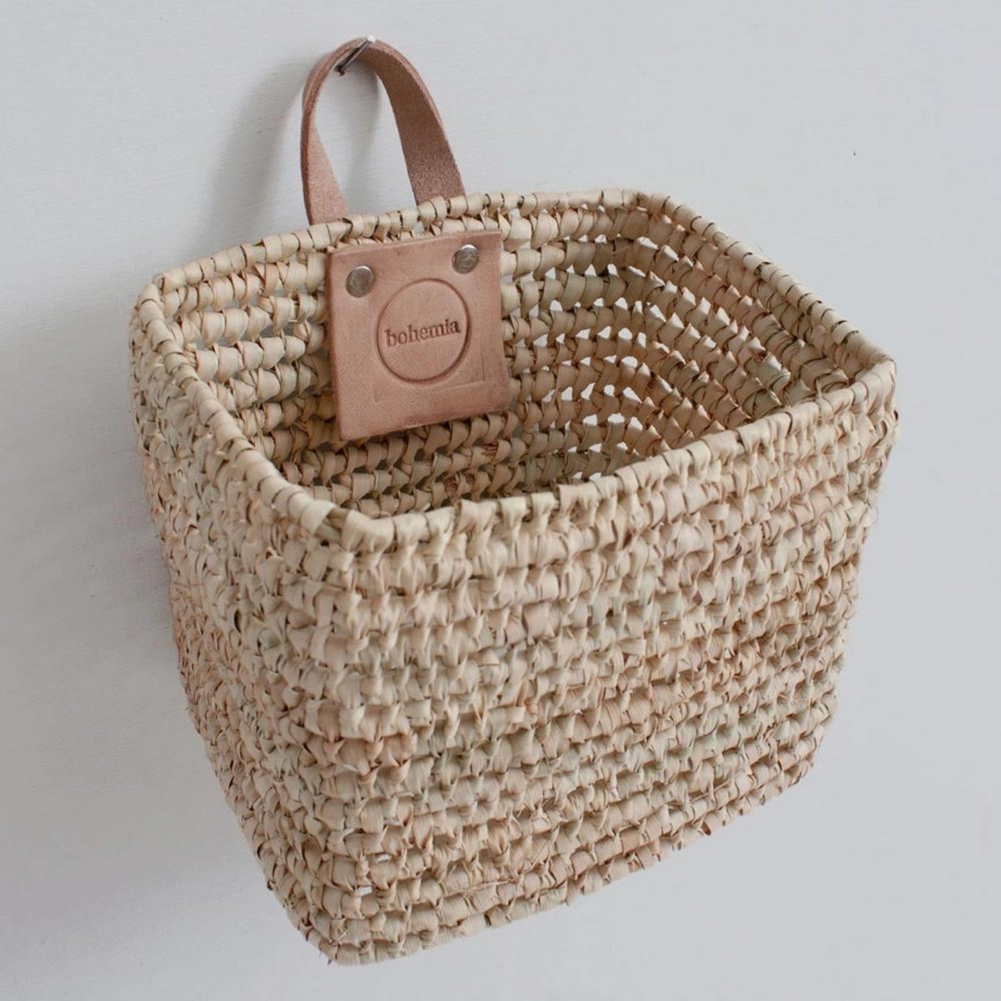A square basket with leather handle hanging from the wall.