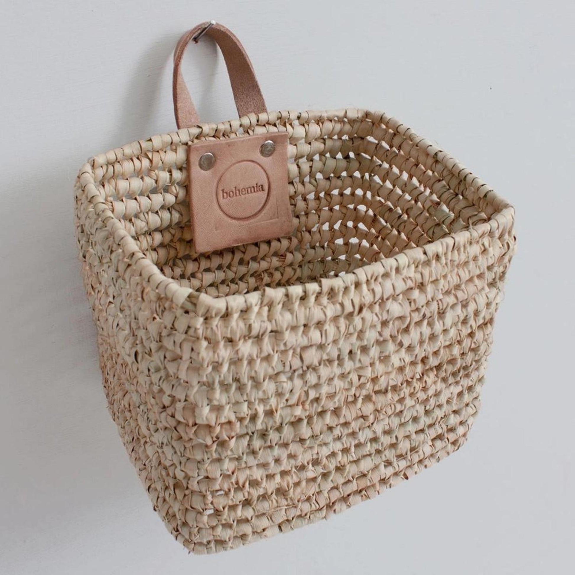 A square basket with leather handle hanging from the wall.