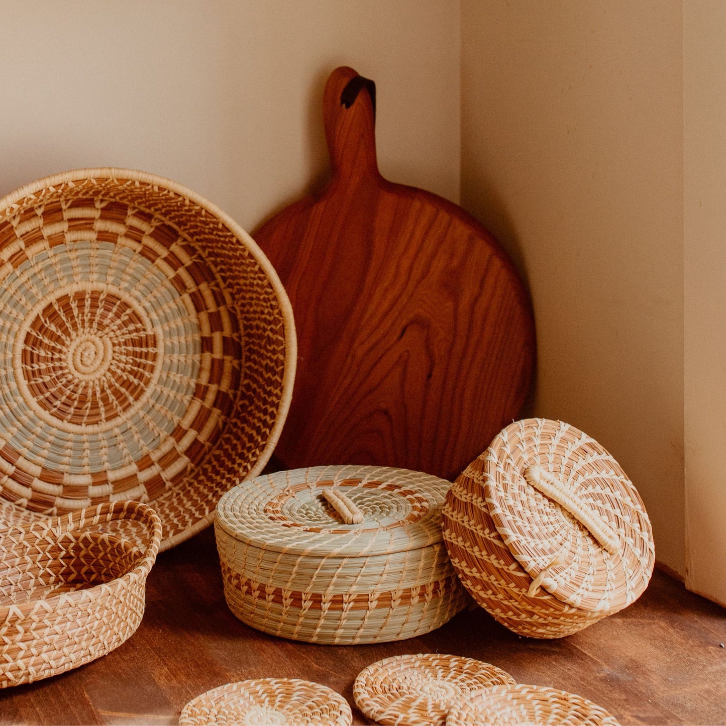 Different sized pine needle baskets and coasters with a wooden cutting board in the background.