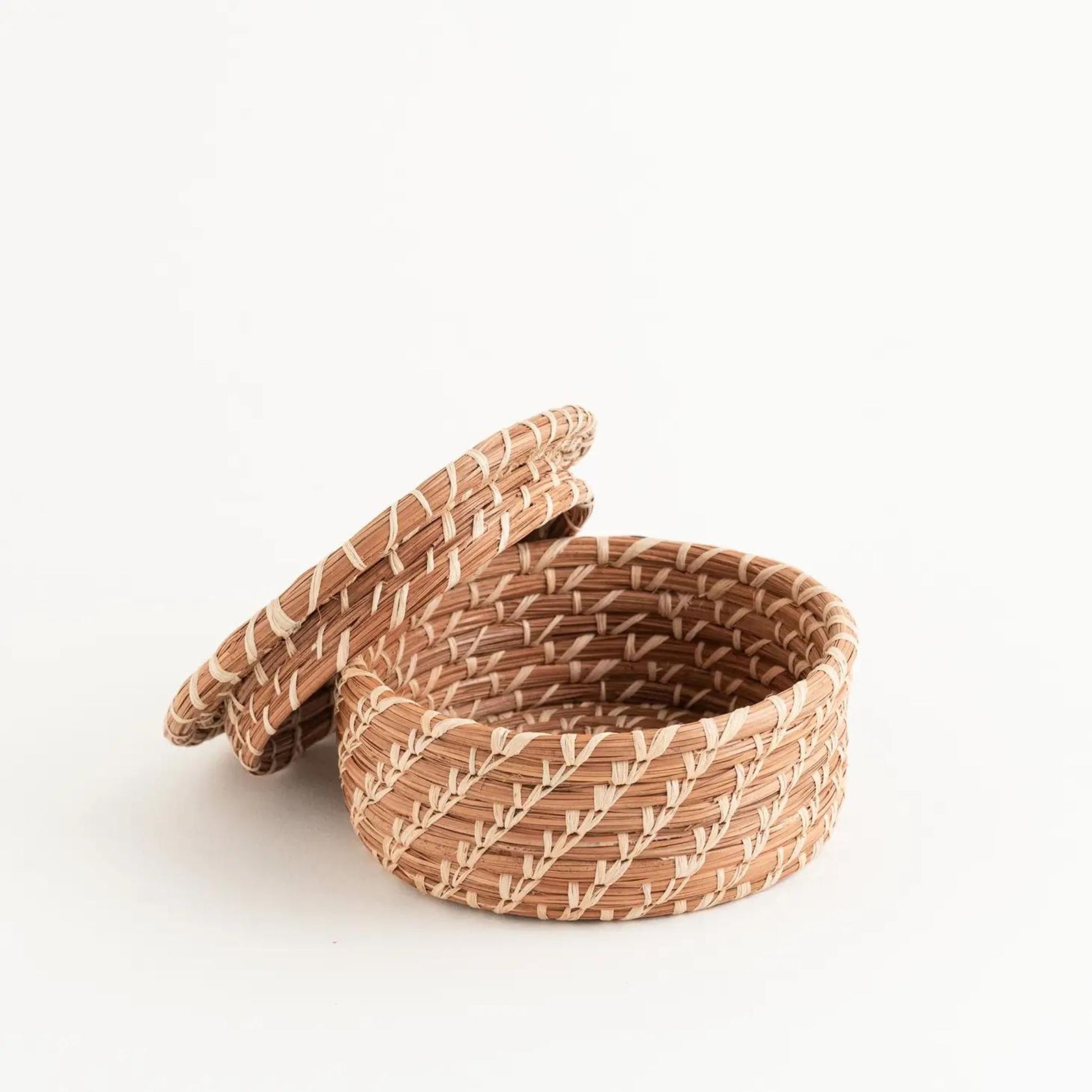 Small woven pine needle lidded basket with lid leaning against the basket.